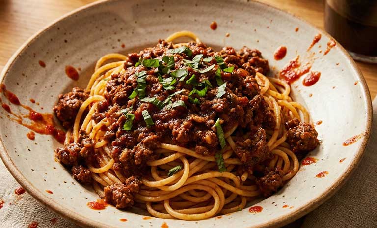 Montagne de spaghetti avec une sauce viande rouge foncé et basilique